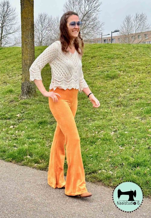 vrouw loopt buiten met een oker gele flared pants high waist langs een groene gras berg