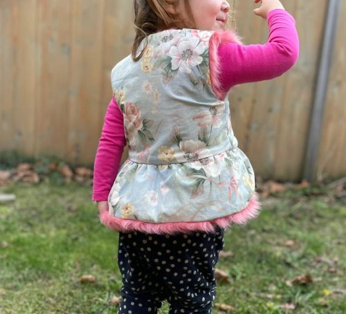 lachende peuter met een bodywarmer aan met Ruffels aan de onderkant buiten spelend