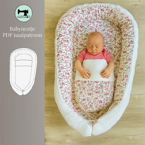 Een bovenaanzicht van een slapende baby in een wit babynestje met een roze bloemenpatroon. De baby draagt een roze shirt en is tot de borst bedekt met een wit dekentje. Het babynestje ligt op een lichte houten vloer.