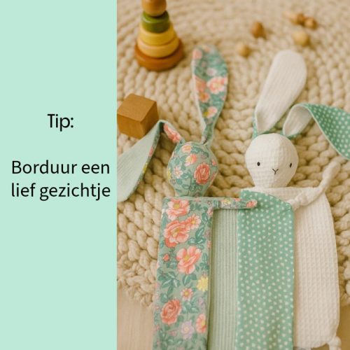 De afbeelding toont twee handgemaakte konijnenknuffeldoekjes die op een geweven, lichtgekleurde mat liggen. Aan de linkerkant is er een konijn gemaakt van een stof met een bloemenpatroon in groen- en roze tinten. De oren hangen slap en het lijfje is plat. Aan de rechterkant is er een ander konijn gemaakt van een witte, gestructureerde stof (mogelijk wafelstof) met groene stof met stippen voor de oren. Dit konijn heeft geborduurde ogen en een eenvoudige mond, wat het een vriendelijk gezicht geeft. Links van de konijnen is een licht turkoois overlay met witte tekst die "Tip:" zegt, gevolgd door "Borduur een lief gezichtje", wat duidt op een tip met betrekking tot het maken van deze items. Op de achtergrond, onscherp, zijn enkele houten babyspeeltjes te zien, waaronder een stapeltoren en enkele houten blokken, wat de context van babyartikelen versterkt.
